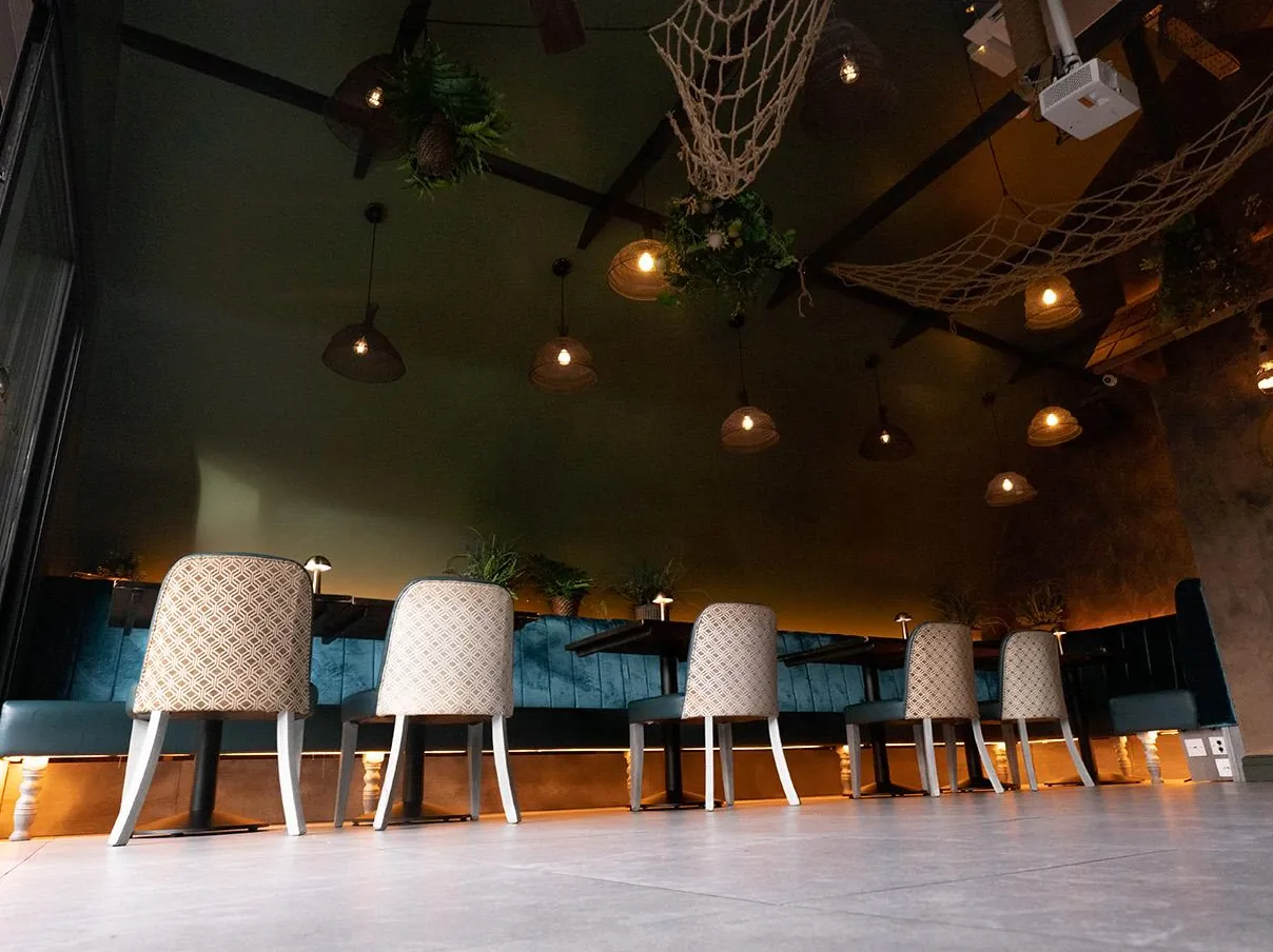 Chairs along the teal velvet banquette under warm lights