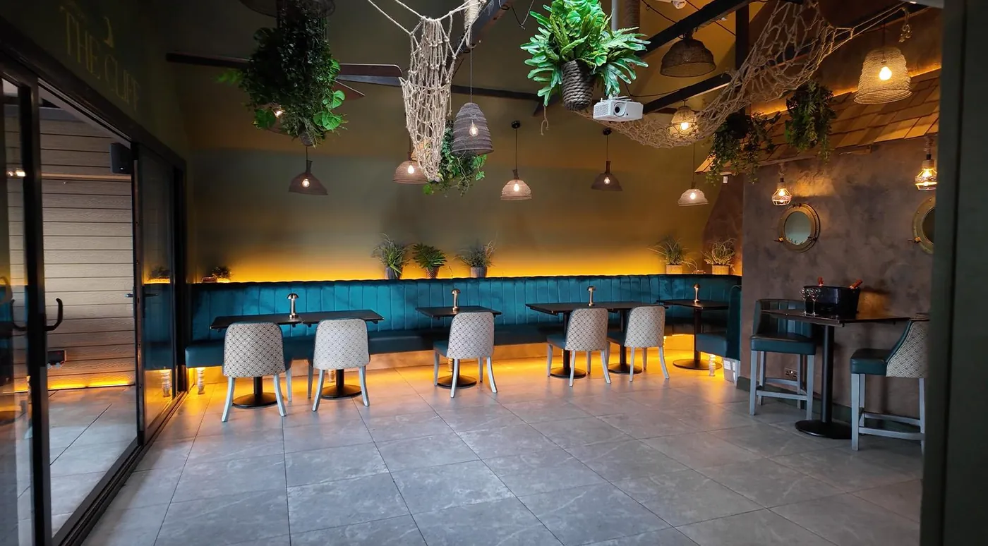 The Cliff lit in amber, with velvet banquettes and hanging greenery